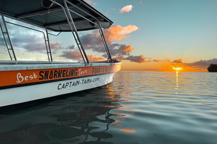 Boat on calm water at sunset with orange sky and clouds.