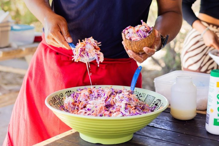 Person serving salad from a large bowl at an outdoor setup.