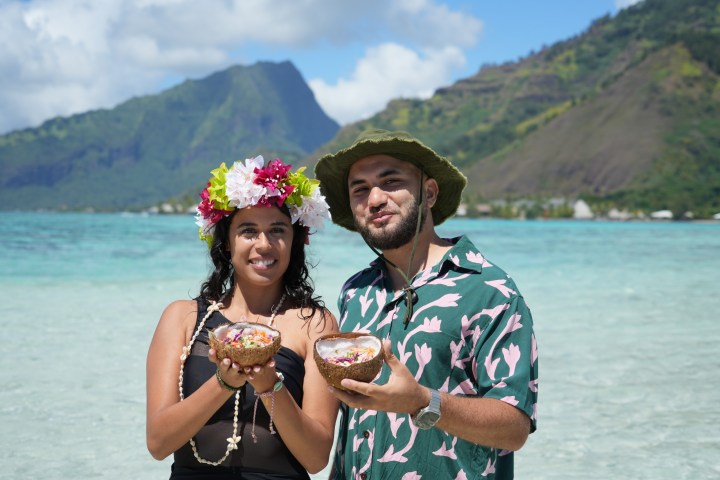 Two people holding food bowls with tropical mountain view.